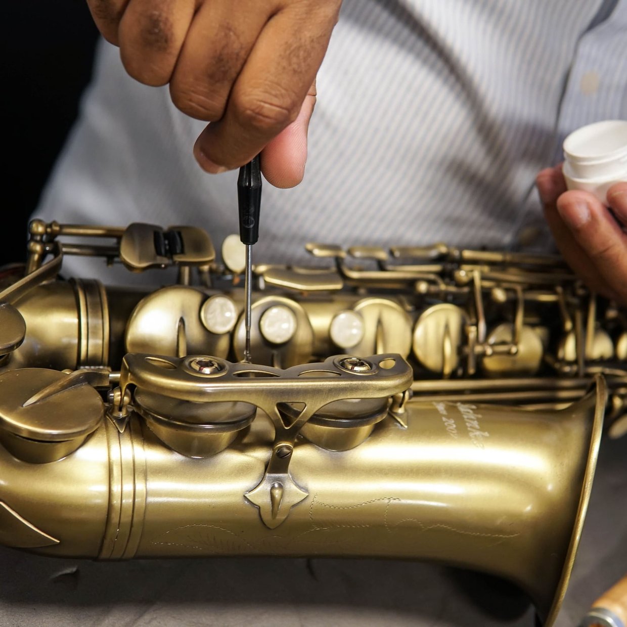 A repair tech adjusting the keys on a brass saxophone