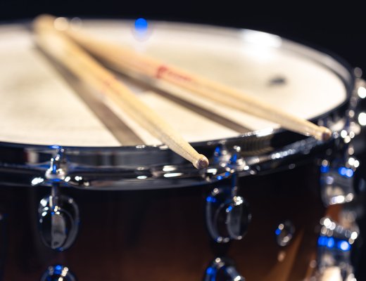 Two drumsticks resting on a sunburst snare drum